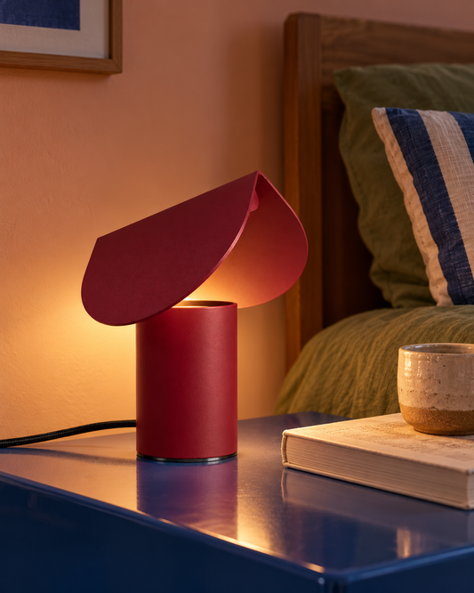 Lampe Biscuit bordeaux allumée sur une table de chevet le soir
