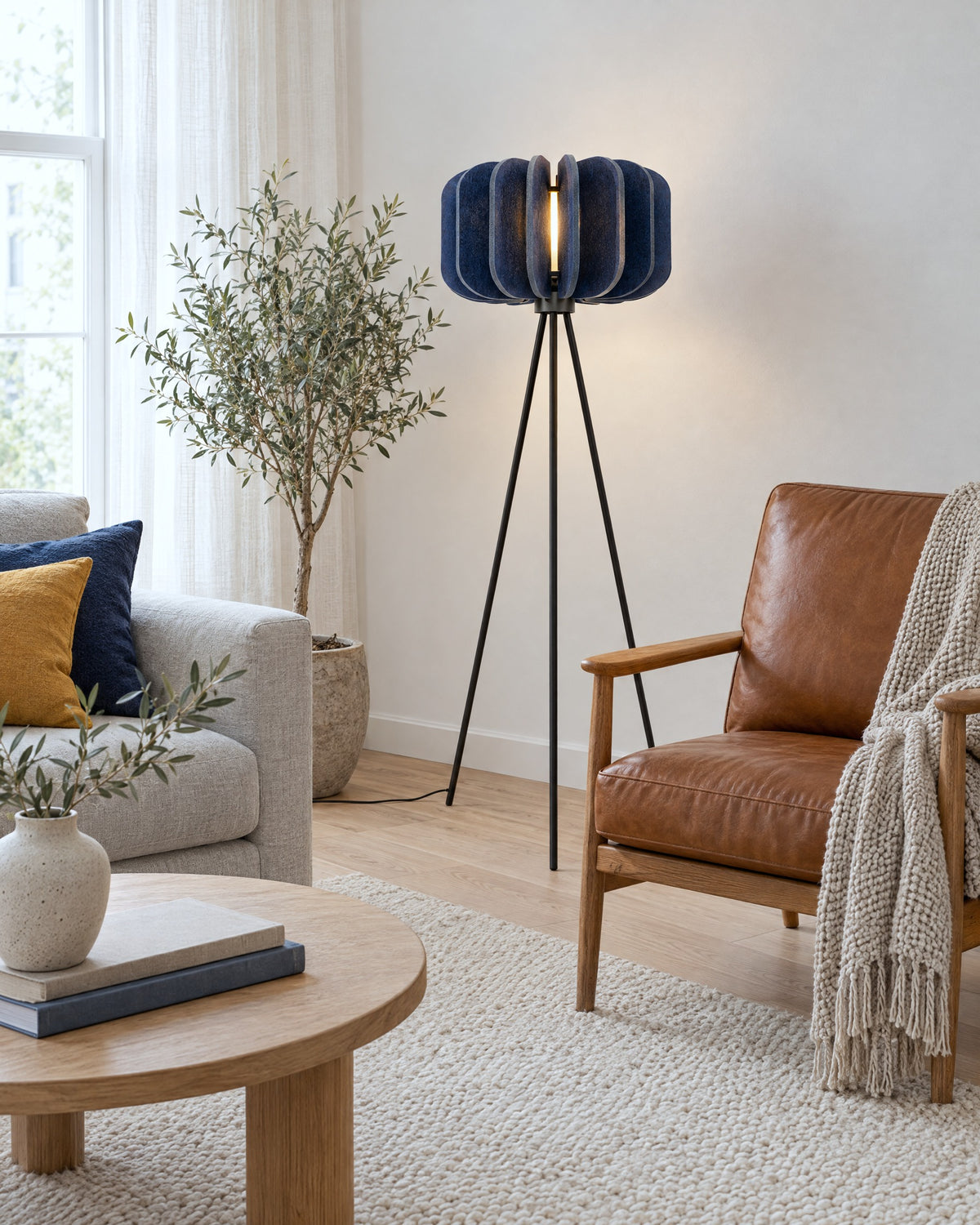 Lampadaire Mula bleu marine à abat-jour en feutre près d'un fauteuil en cuir dans un salon scandinave